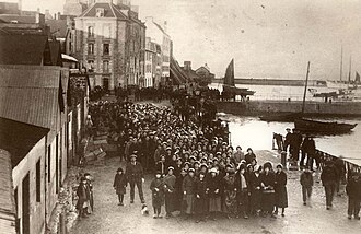 Foule de personnes massée le long d’un petit port maritime.