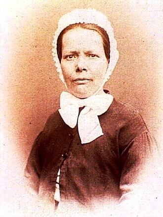 Photo portrait de Nathalie Lemel vue de face de couleur sepia. Elle porte un chapeau blanc avec des lanières blanches nouées en ruban sous le cou et une vareuse.Nathalie Lemel.